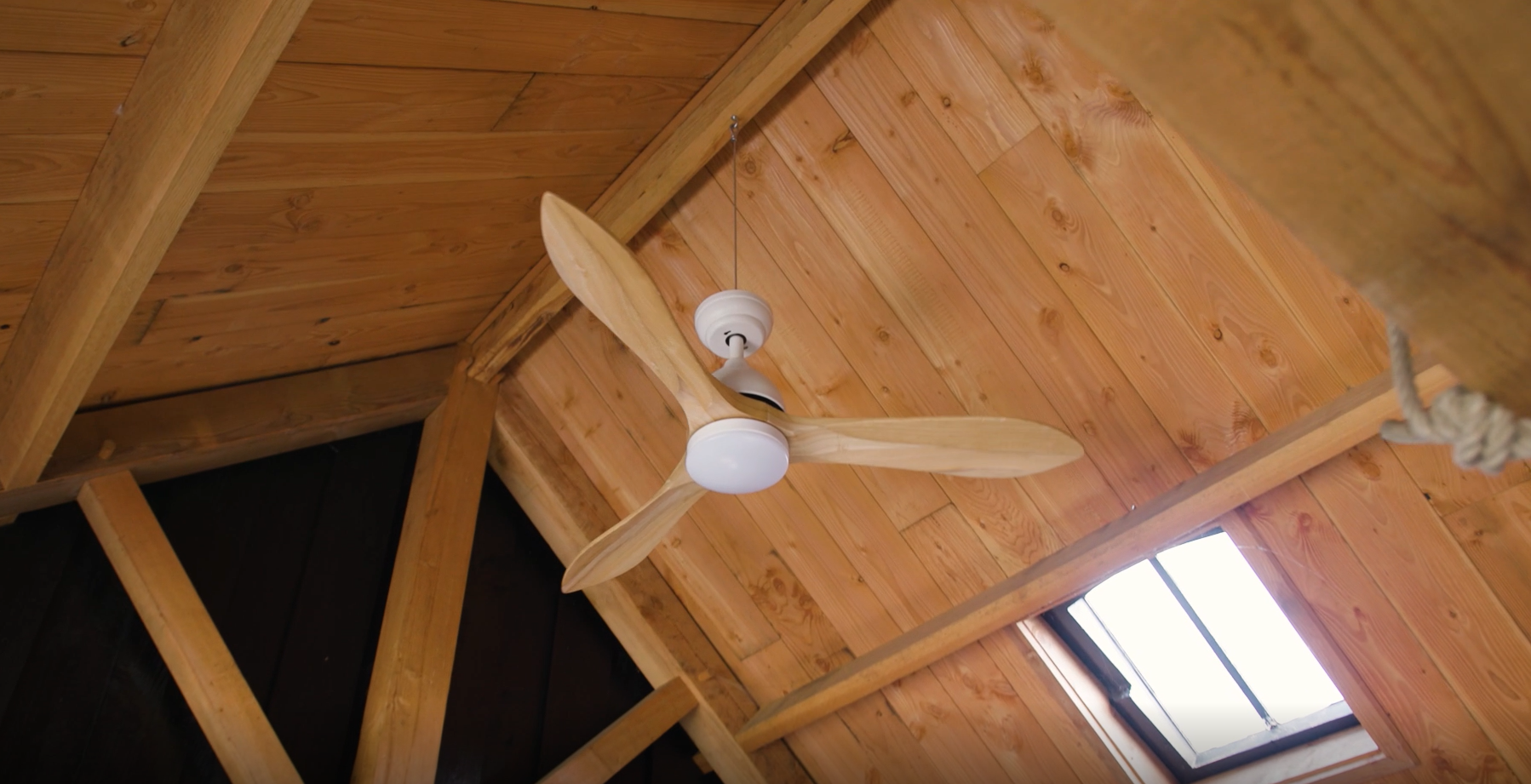 Un ventilatore da soffitto in legno è appeso sotto un soffitto in legno con lucernario.