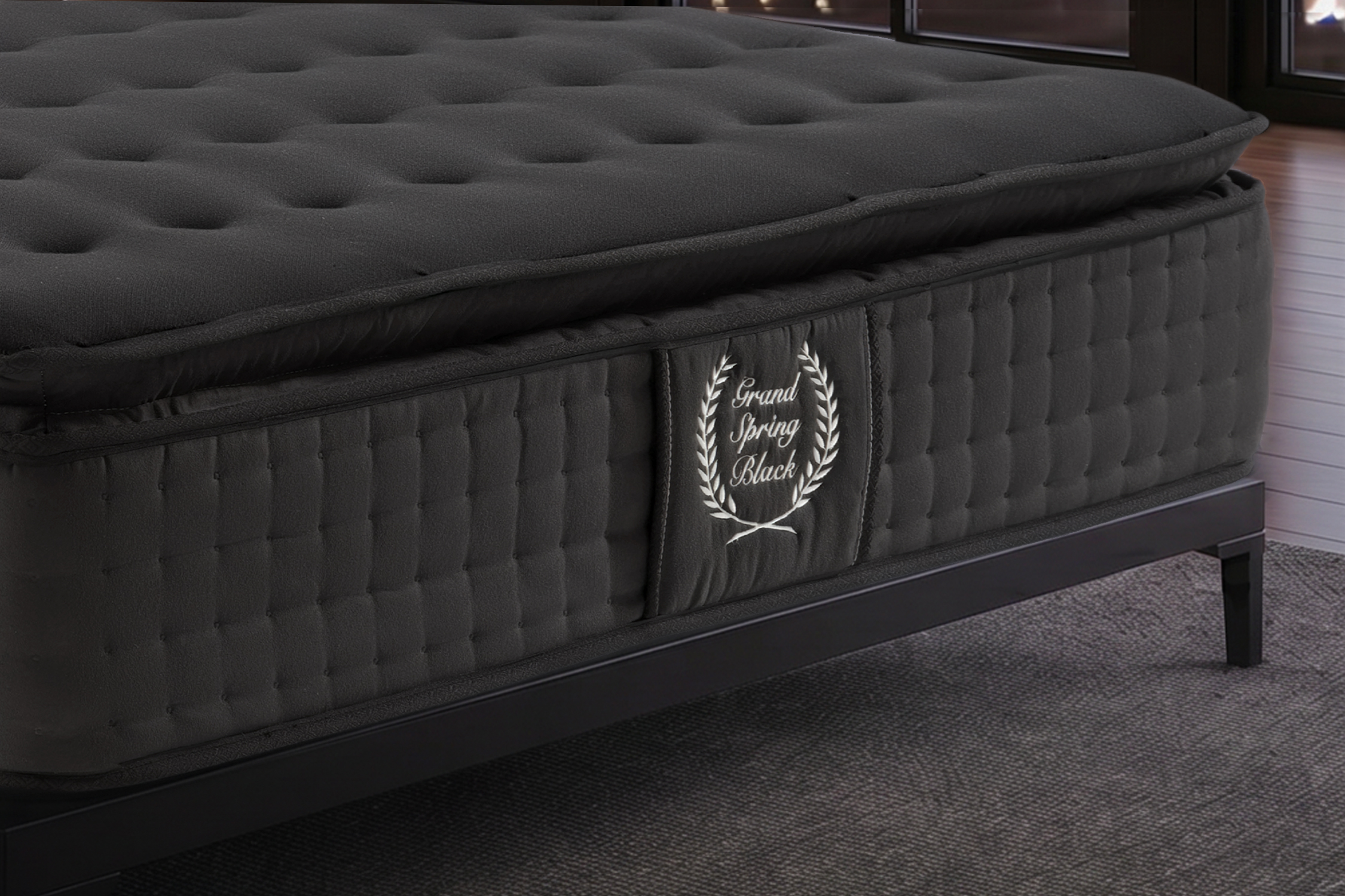 Un colchón de box spring negro con superficie acolchada y logo de corona de laurel.