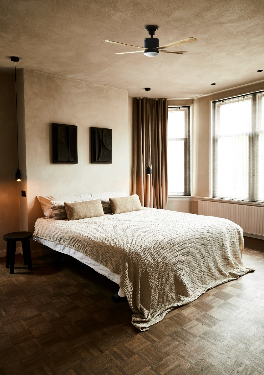 Una camera da letto con letto, ventilatore a soffitto, quadri e pavimento in legno.