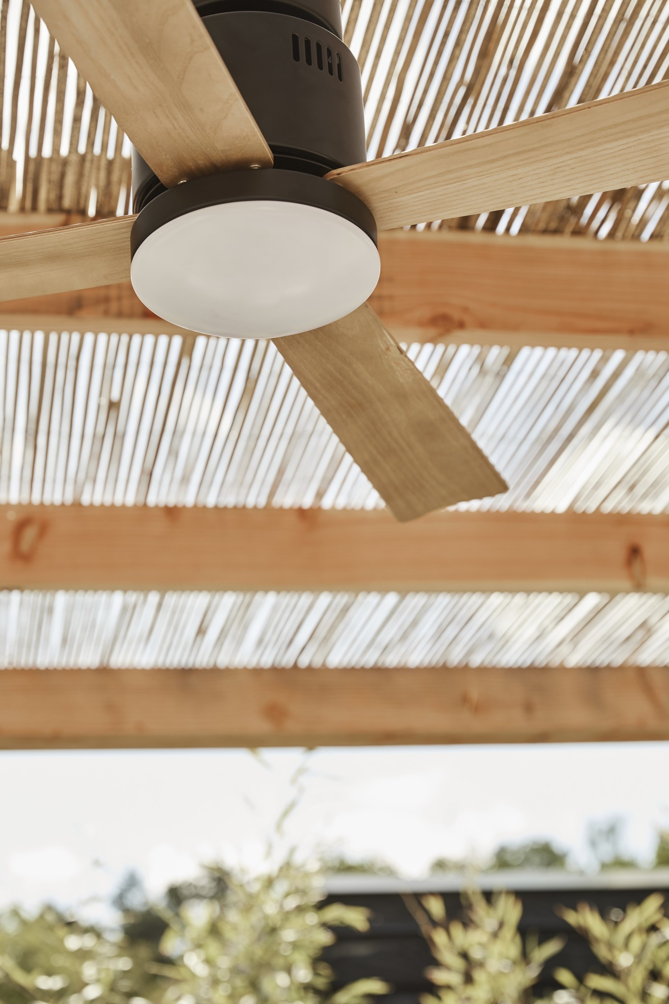 Un ventilatore da soffitto scuro con pale in legno sotto un tetto di bambù.