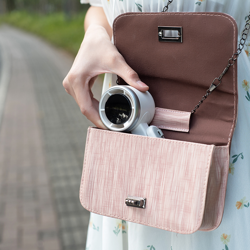 Eine Hand legt einen kleinen weißen Lüfter in eine rosafarbene Tasche.