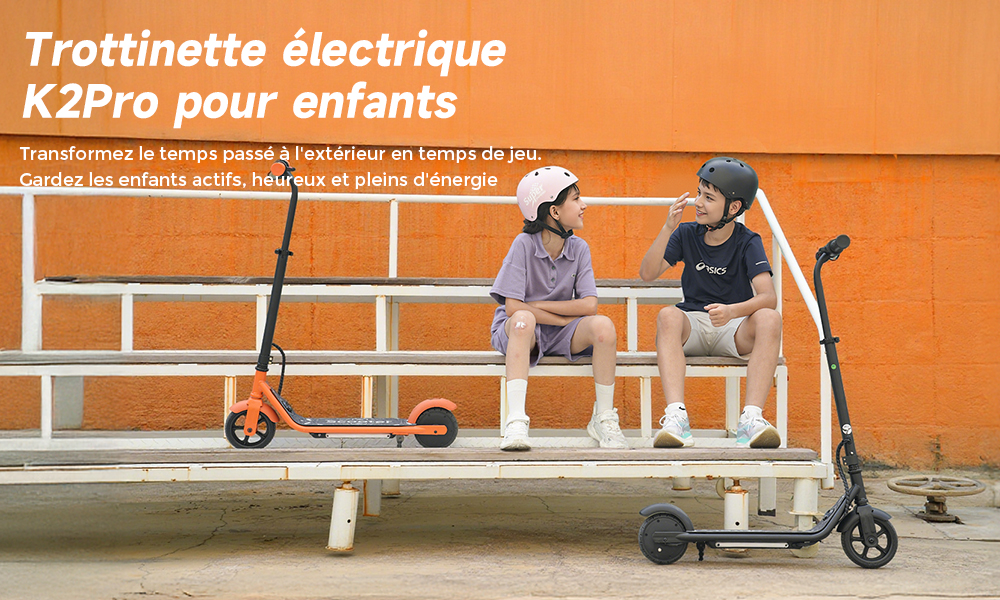 Due bambini seduti su gradinate accanto a monopattini elettrici, muro arancione dietro.