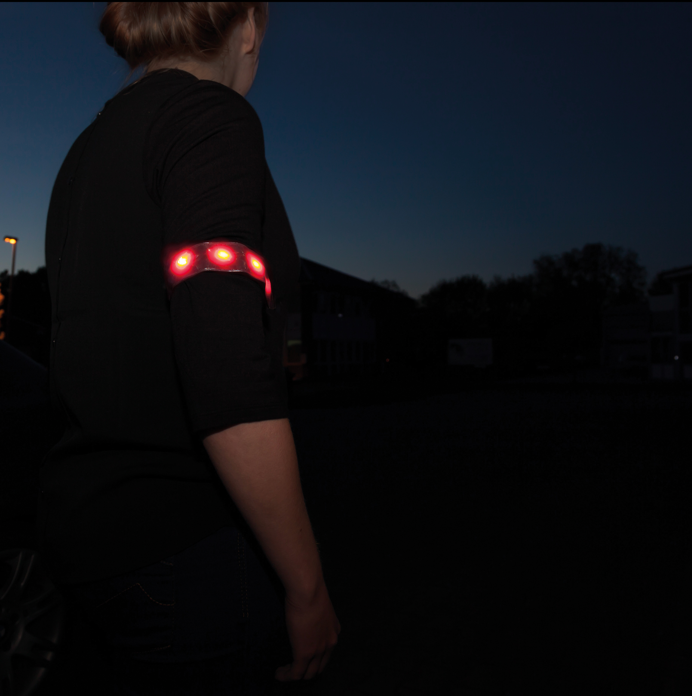 Person mit schwarzem Oberteil und rotem LED-Armband im Dunkeln.