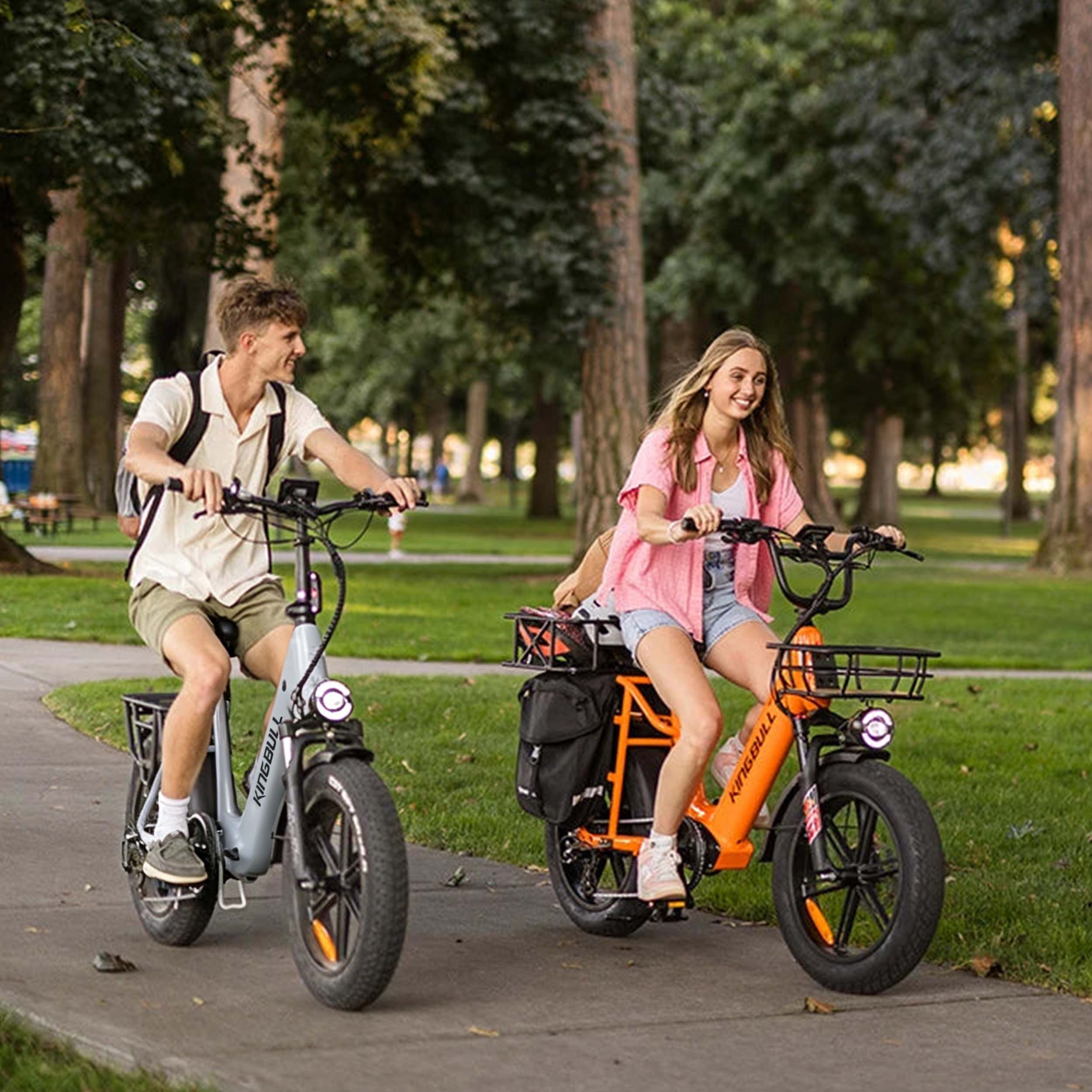 Ein Mann und eine Frau fahren E-Bikes auf einem Weg im Park, Bäume im Hintergrund.