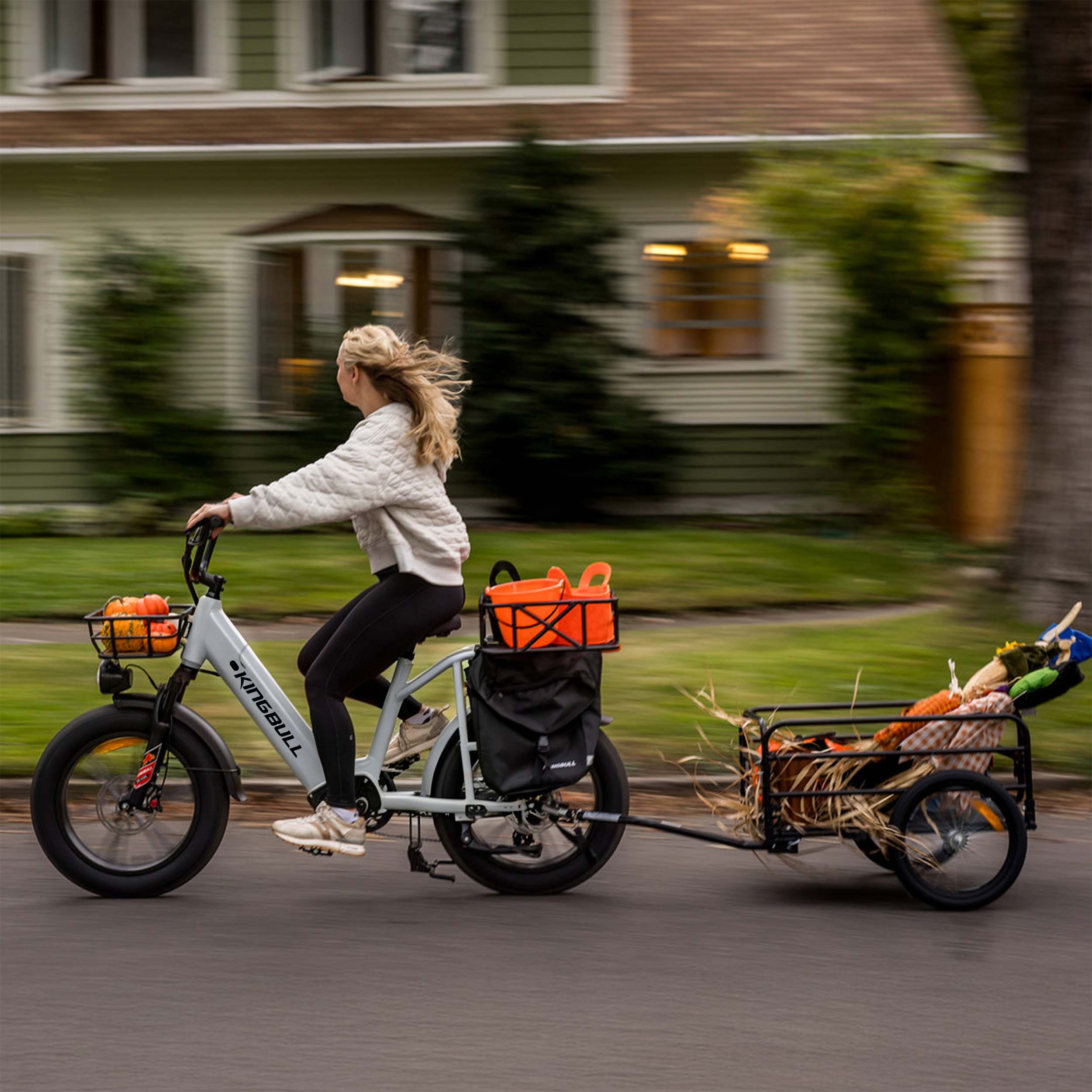 Eine Frau fährt ein E-Bike mit Kürbissen und einem Anhänger mit einer Vogelscheuche.