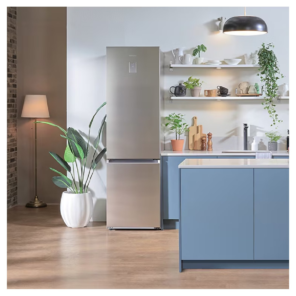 Moderne zilveren koelkast naast blauwe keukenkastjes, lamp en plant.