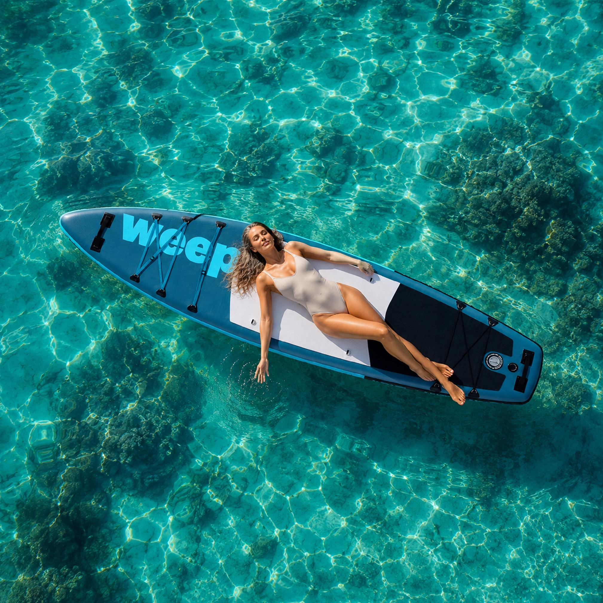 Kobieta leży na desce surfingowej w turkusowej wodzie nad koralem.