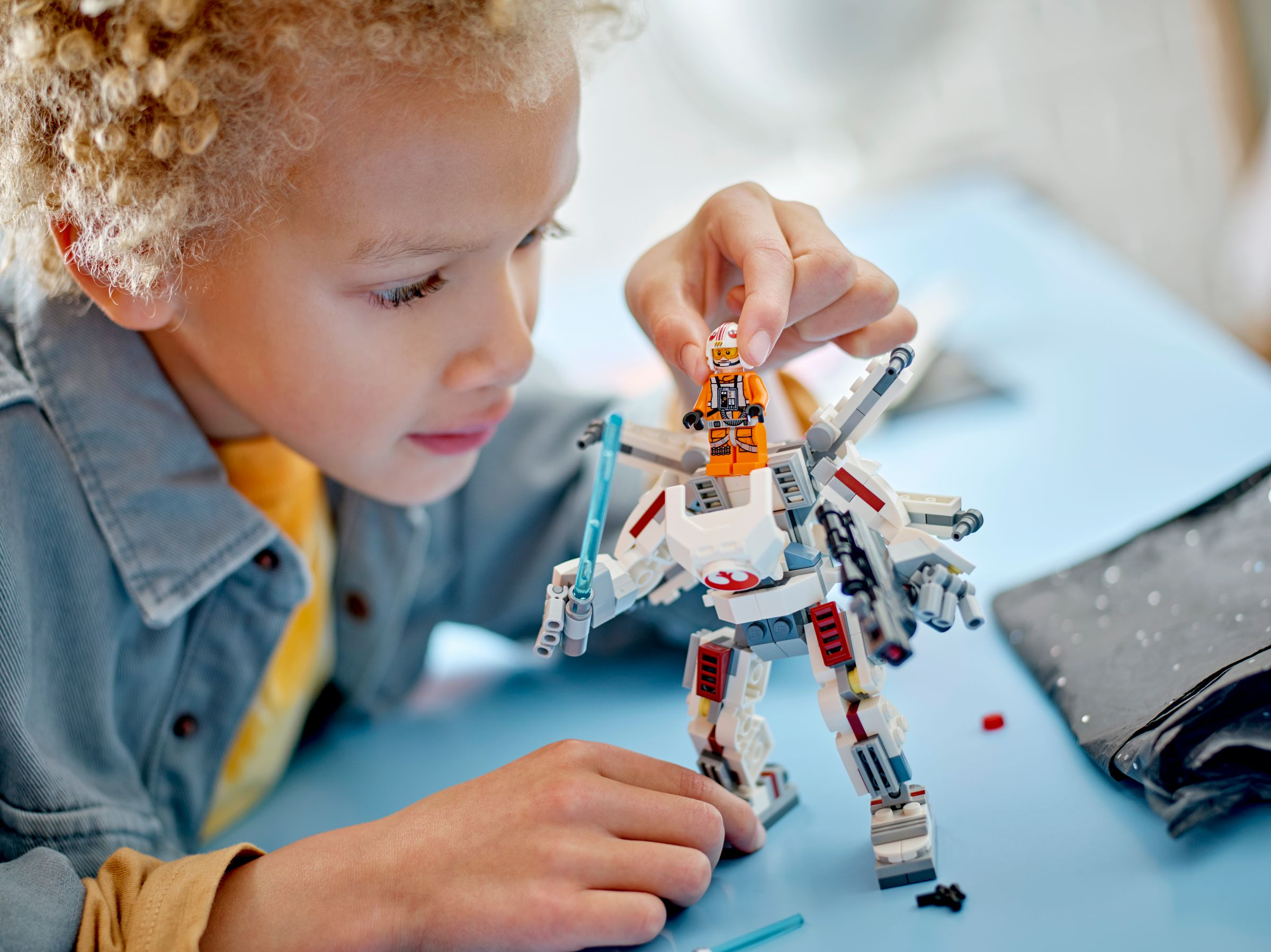 Ein Junge spielt mit einem weißen Lego-Roboter und einer orangefarbenen Figur.