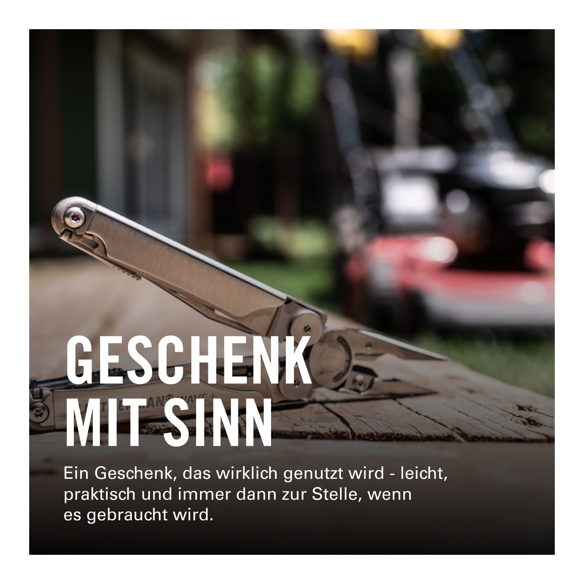 Ein Multitool liegt auf einem Holzbrett, im Hintergrund ein Rasenmäher.