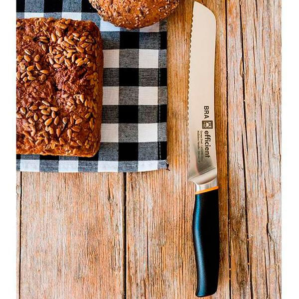 Un cuchillo de pan dentado con mango negro descansa junto a una hogaza y un bollo sobre un paño a cuadros.