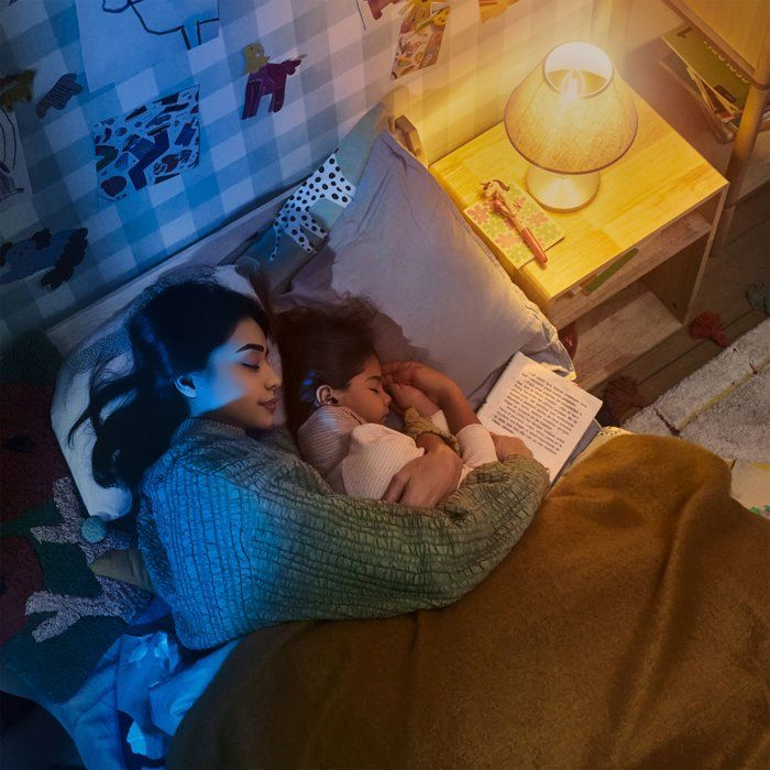 Madre e figlia dormono a letto, libro e abat-jour.