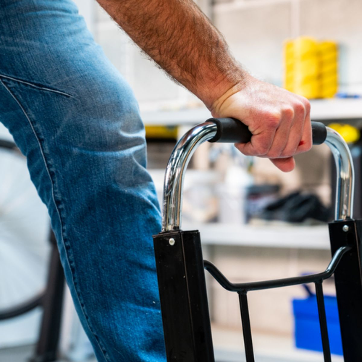 Uomo in jeans afferra un carrello con manico cromato, sfondo sfocato.