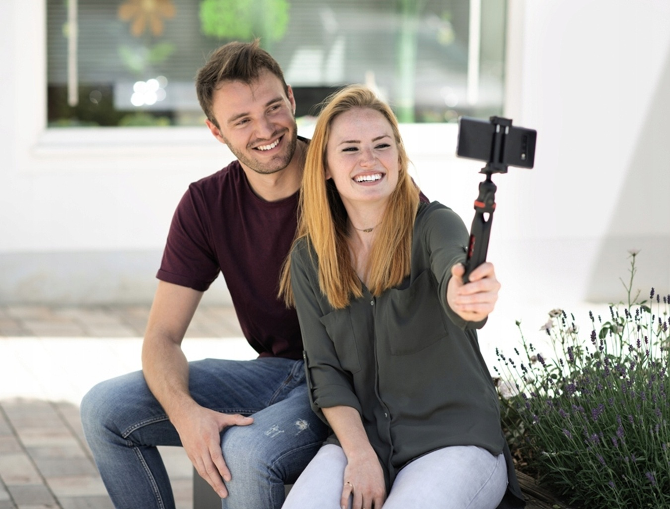Ein lächelndes Paar macht draußen ein Selfie mit einem Smartphone am Selfie-Stick.