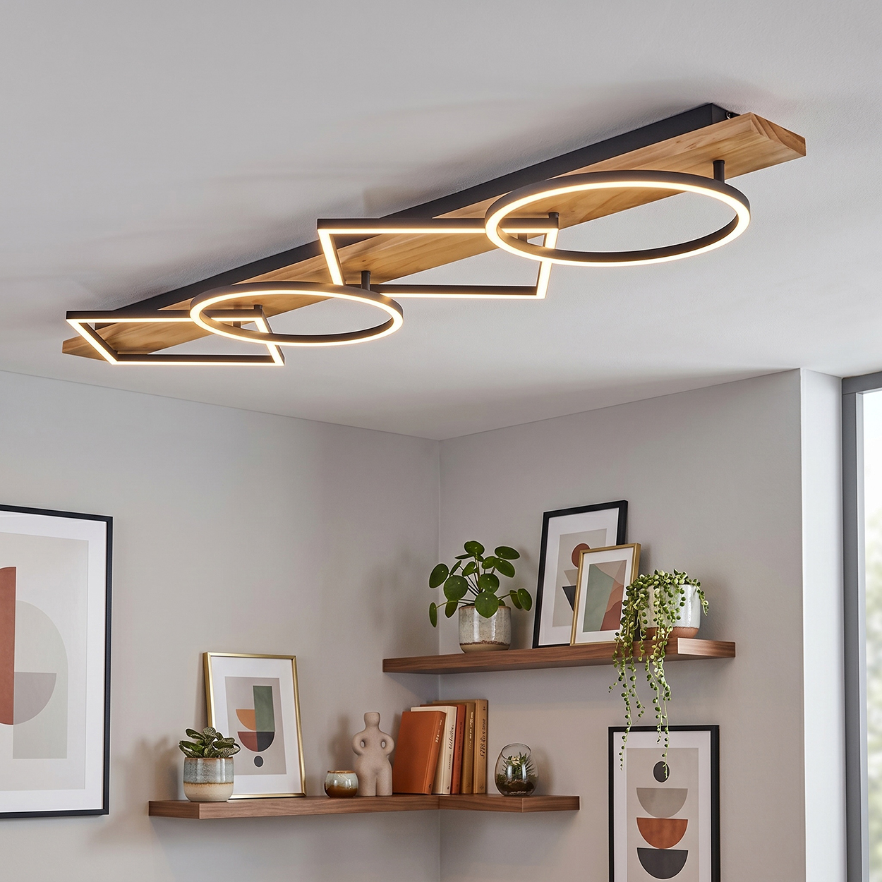 Eine Deckenleuchte mit Holzsockel und geometrischen Ringen aus Metall mit LED-Beleuchtung.