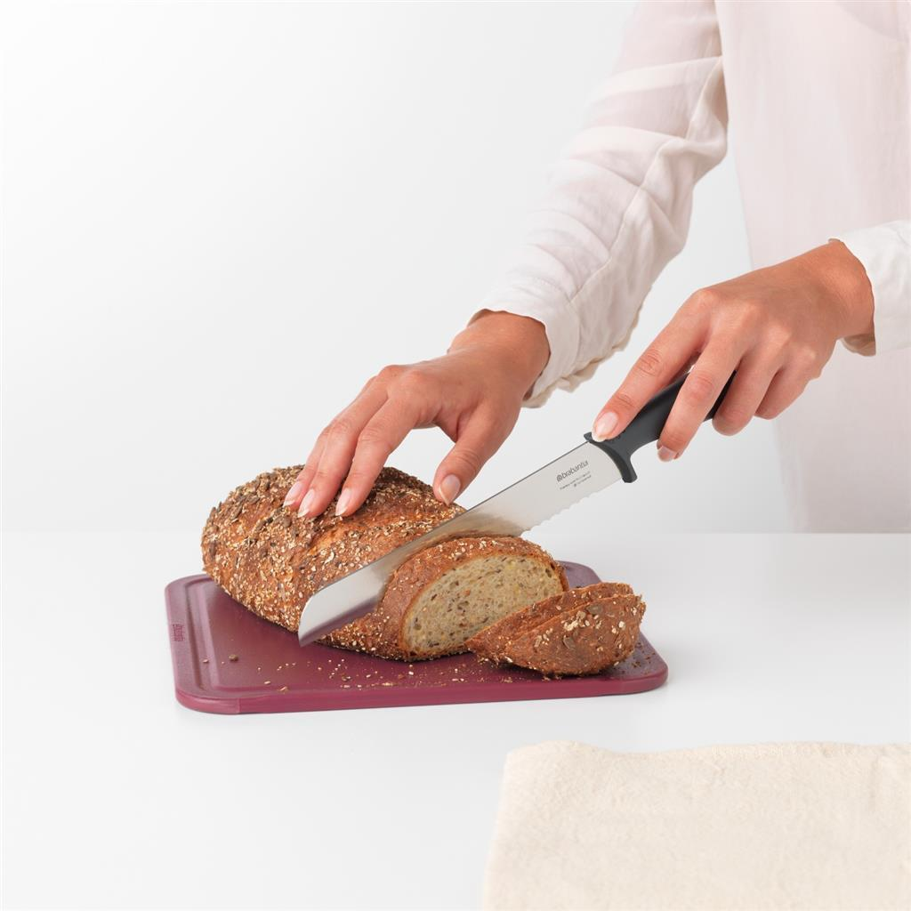 Una persona affetta una pagnotta con un coltello da pane su un tagliere.