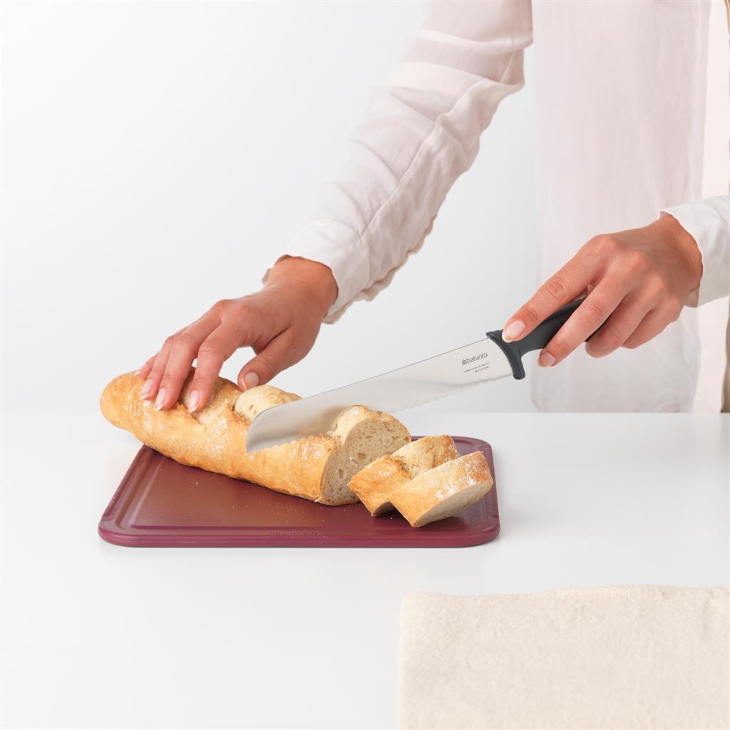 Una persona affetta una baguette su un tagliere viola con un coltello da pane.