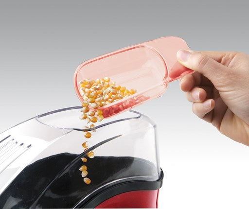 Ein Löffel mit Maiskörnern wird über eine Popcornmaschine gegossen.