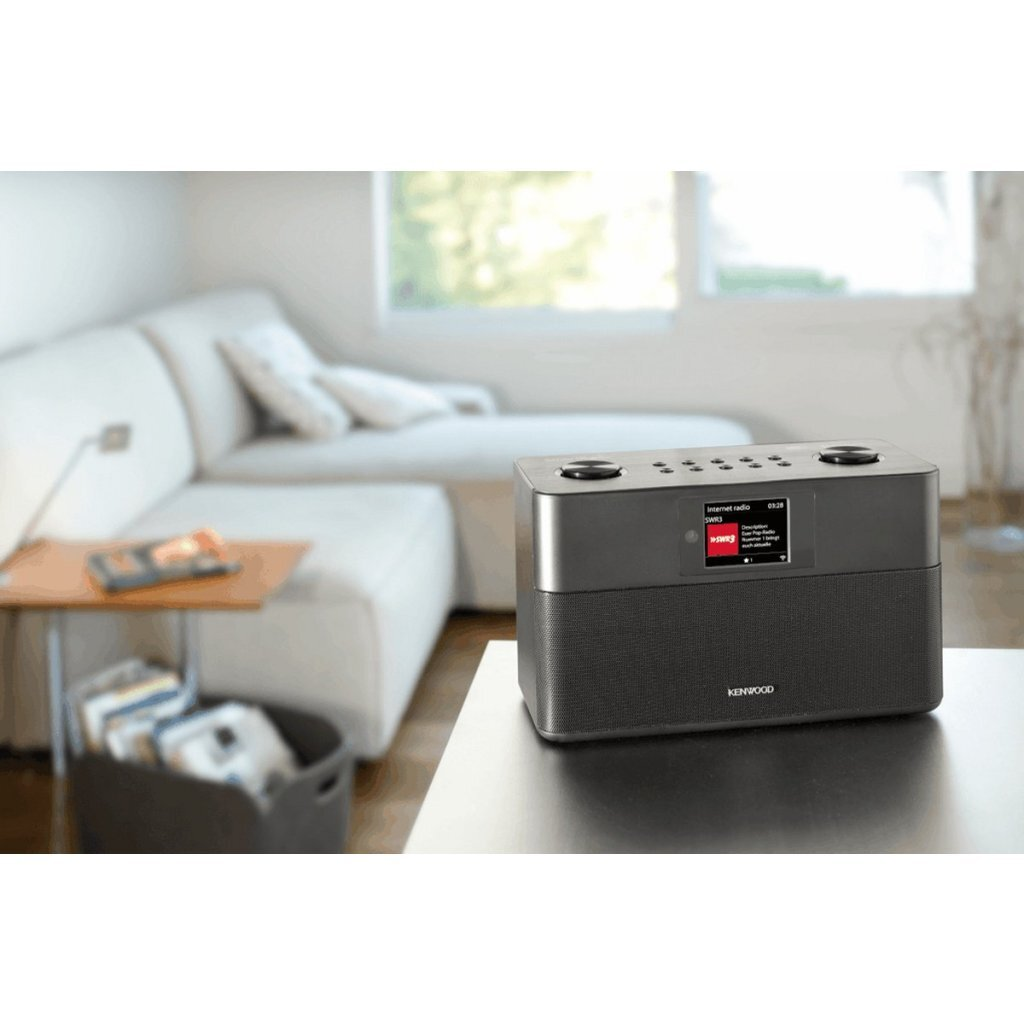 Une radio internet Kenwood est posée sur une table devant un canapé flou.