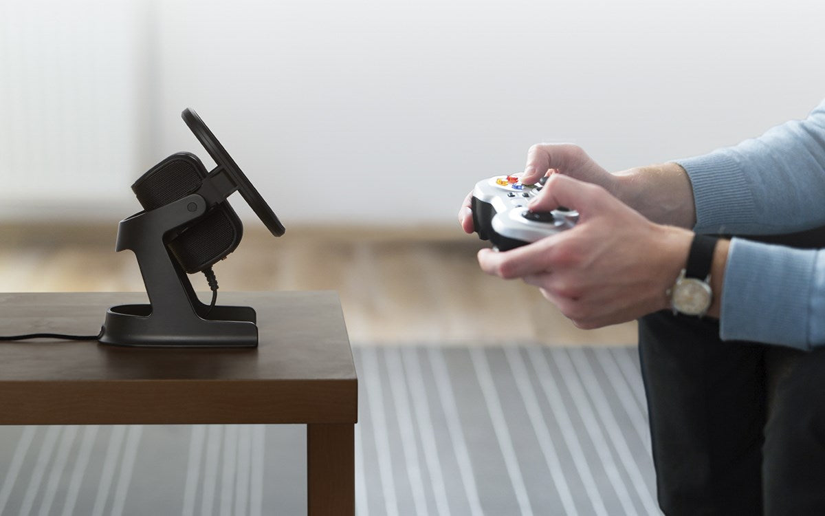 Persona gioca con un controller, supporto per cuffie sul tavolo.