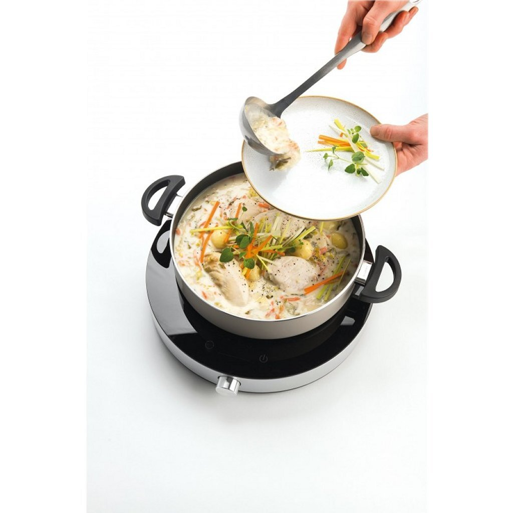 Un cucharón saca sopa cremosa a un plato con tiras de verduras decoradas.