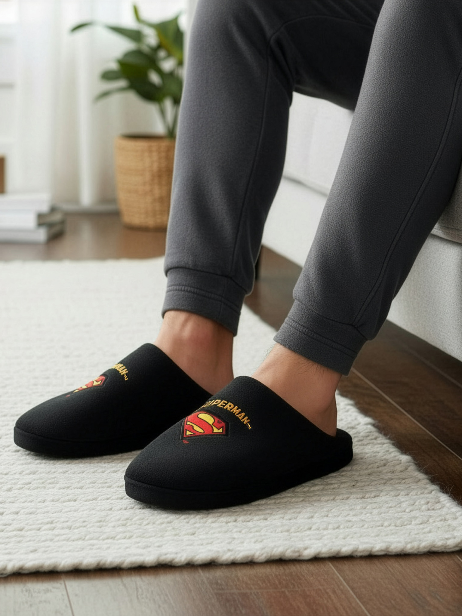 Schwarze Hausschuhe mit Superman-Logo auf weißem Teppich.