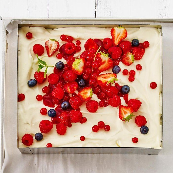 Una torta quadrata con crema bianca, coperta da molte bacche rosse.