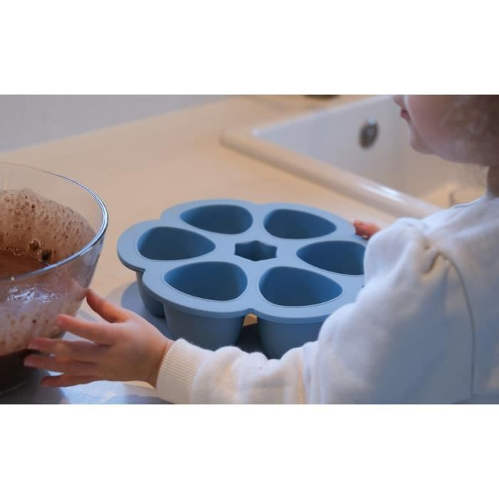 Ein Kind mit einem blauen Blumen-Muffinblech und einer Schüssel mit Teig.