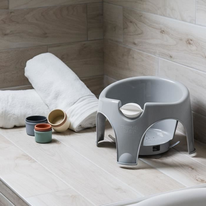 Asiento de baño gris para bebé con dos toallas y tres tazas pequeñas.