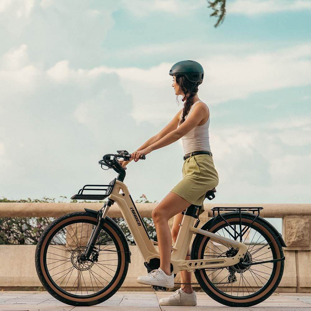 Mujer con casco y shorts monta bicicleta eléctrica beige en sendero pavimentado.