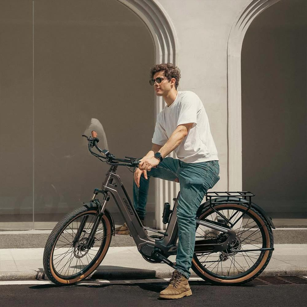 Un hombre se sienta en una e-bike frente a una pared clara con arcos.