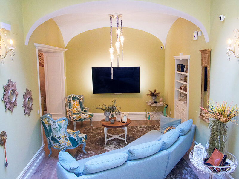 Una sala de estar amarillo claro con sofá azul, sillones estampados y televisor.