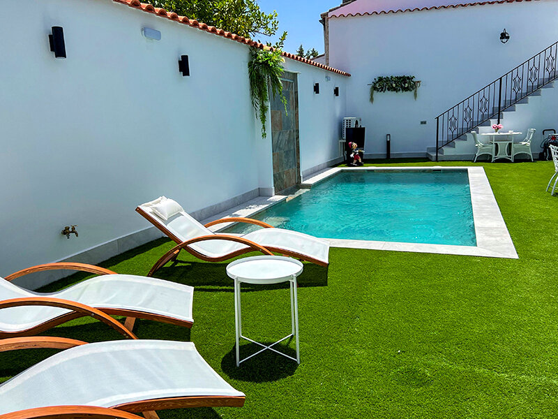 Una piscina pequeña con agua turquesa, rodeada de césped artificial y tumbonas.