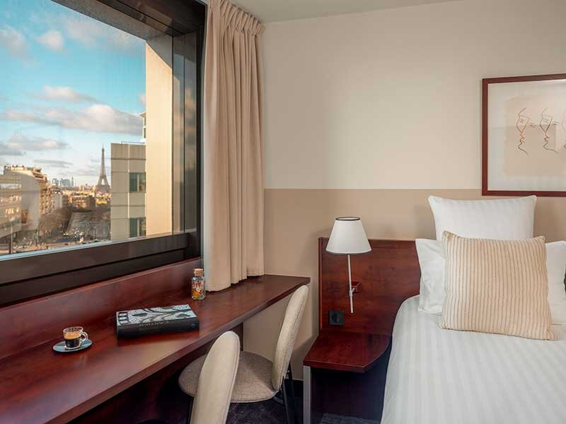 Habitación de hotel con cama, escritorio y vista a la Torre Eiffel.