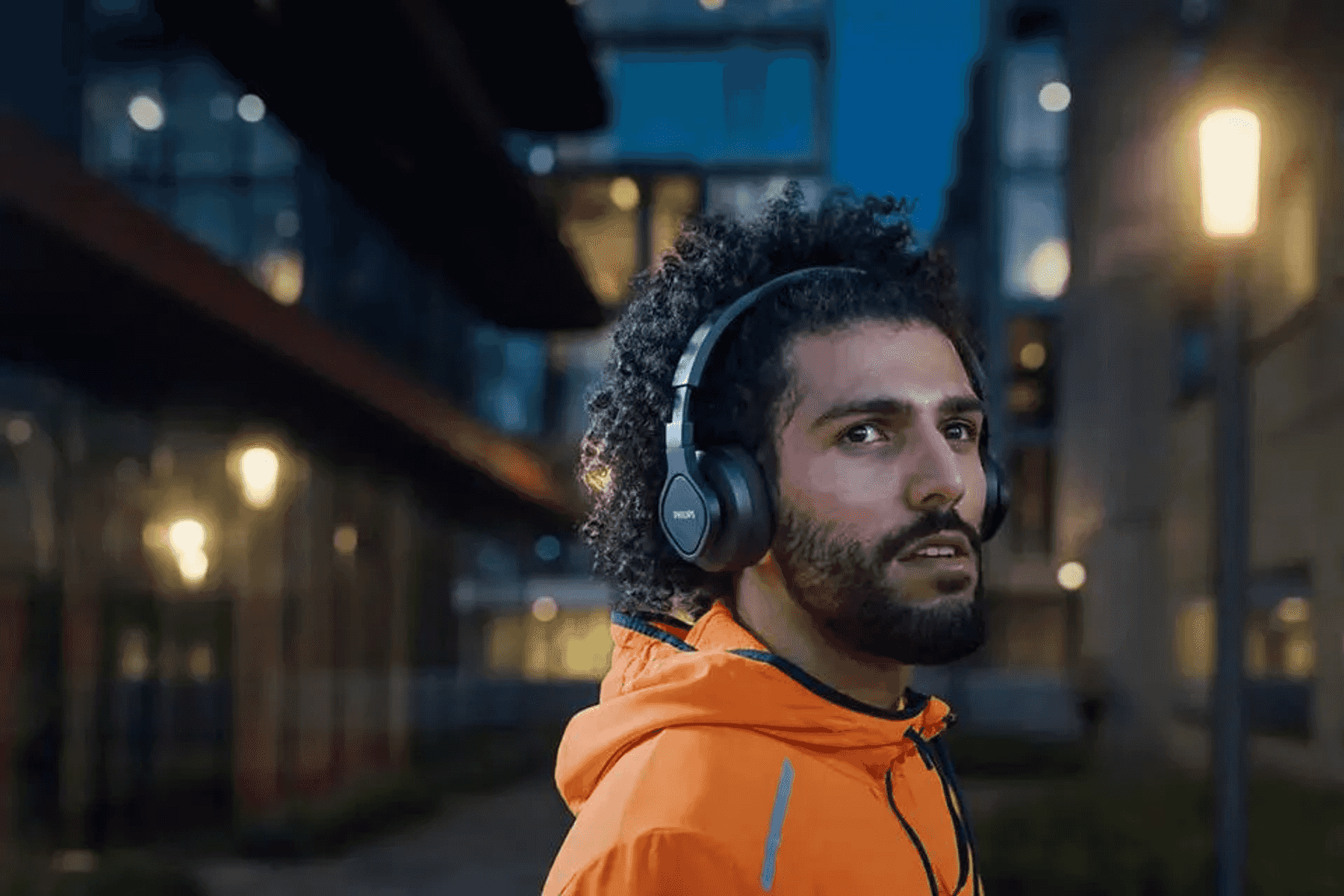 Hombre con auriculares viste chaqueta naranja, de noche en la ciudad.