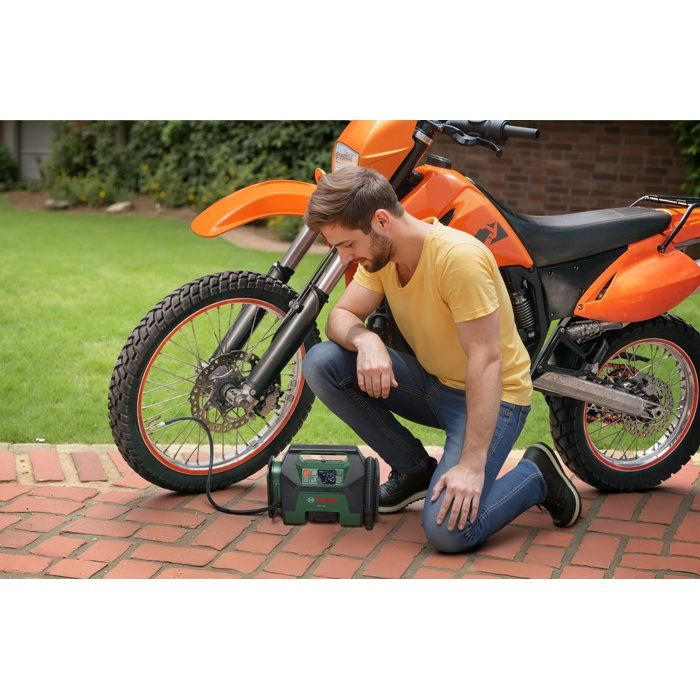 Mann kniet neben orangefarbenem Motorrad und bedient tragbaren Kompressor.