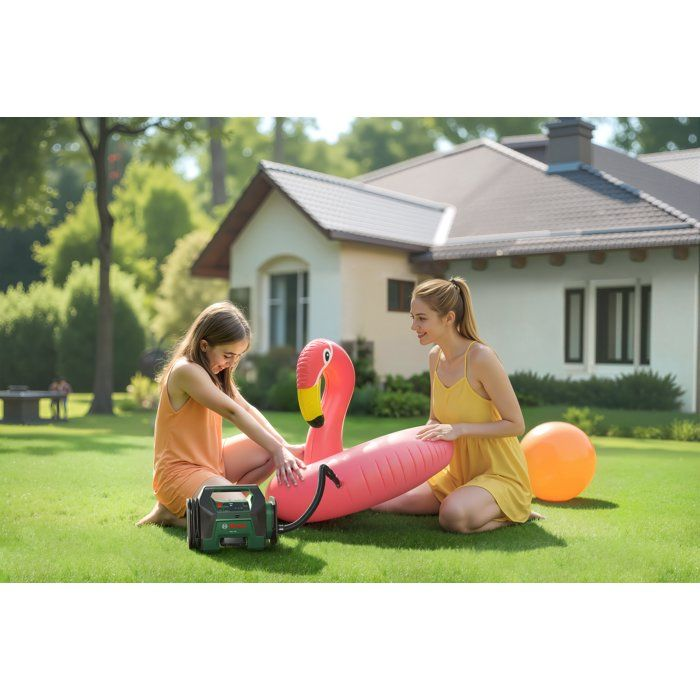 Zwei Mädchen pumpen eine aufblasbare Flamingo-Poolliege auf einem grünen Rasen nahe einem Haus auf.