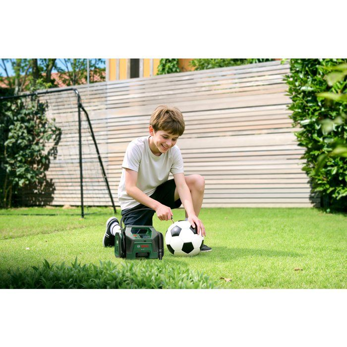 Junge auf einem Rasen pumpt einen Fußball mit einer Luftpumpe auf.