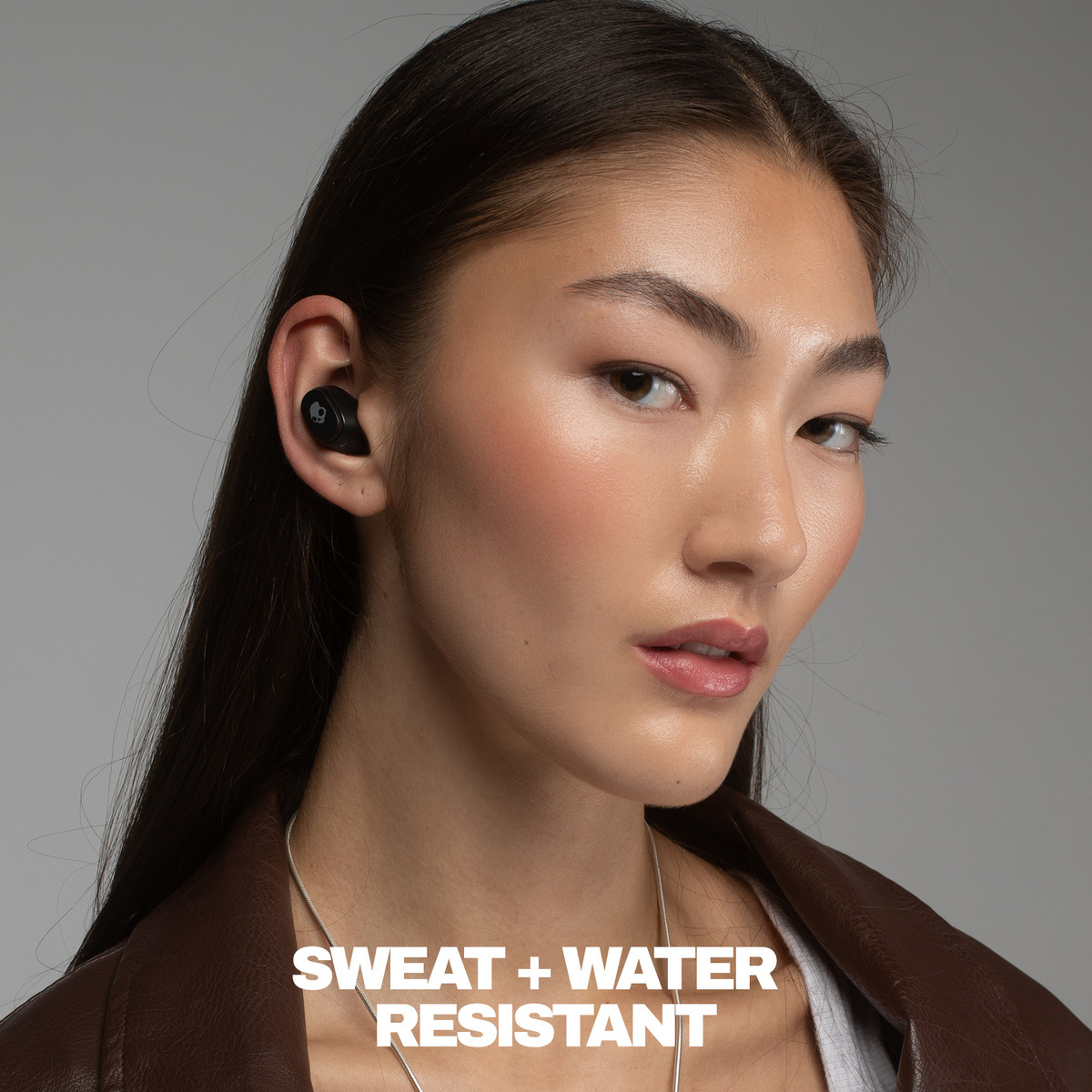 Nahaufnahme einer Frau mit einem schwarzen Ohrhörer, der das Skullcandy-Logo zeigt.