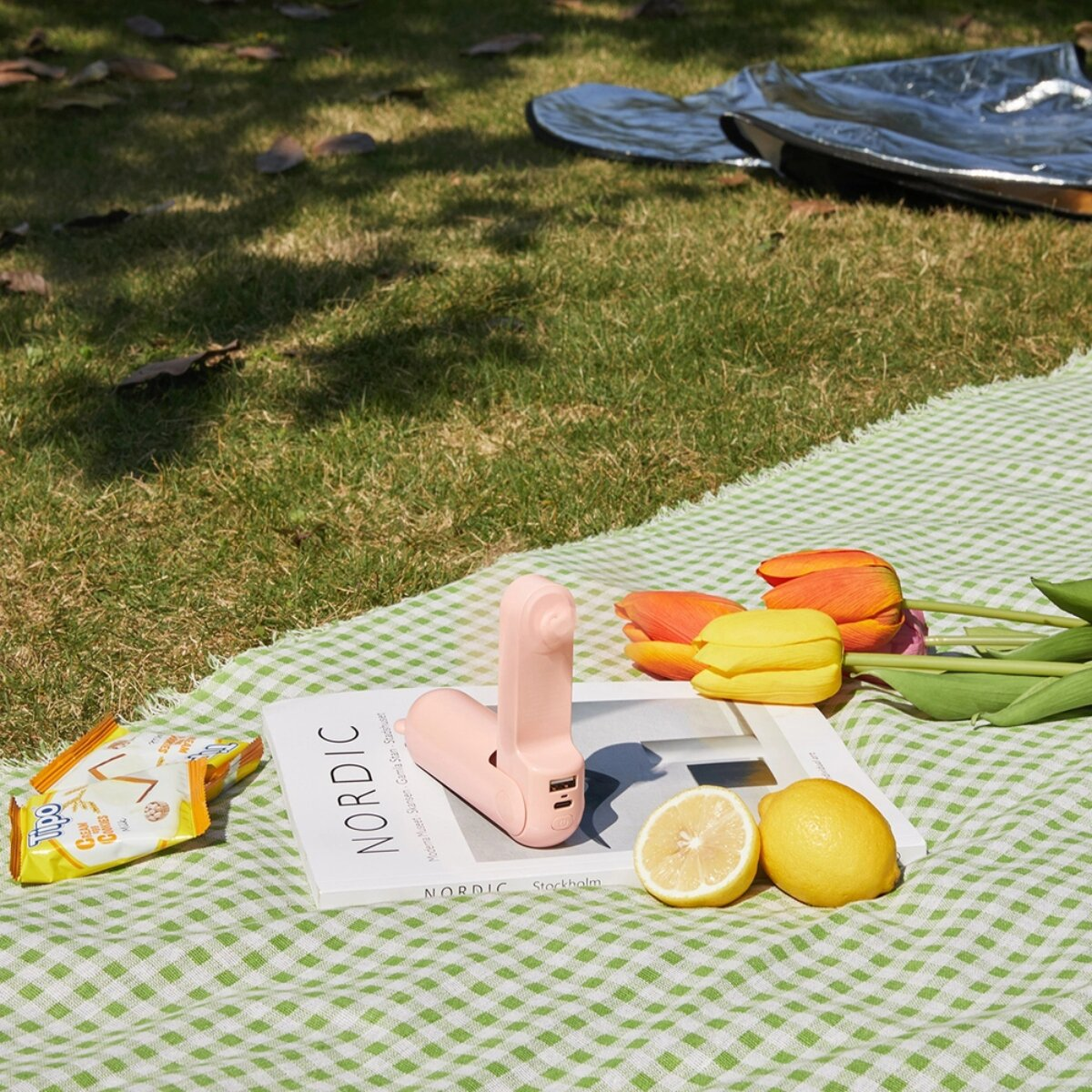 Un ventilatore portatile rosa su un libro vicino a tulipani e limoni.