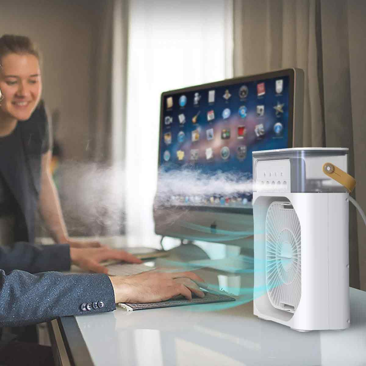 Ein weißer tragbarer Ventilator mit Wassertank steht neben einem Computer auf einem Schreibtisch und sprüht Nebel.