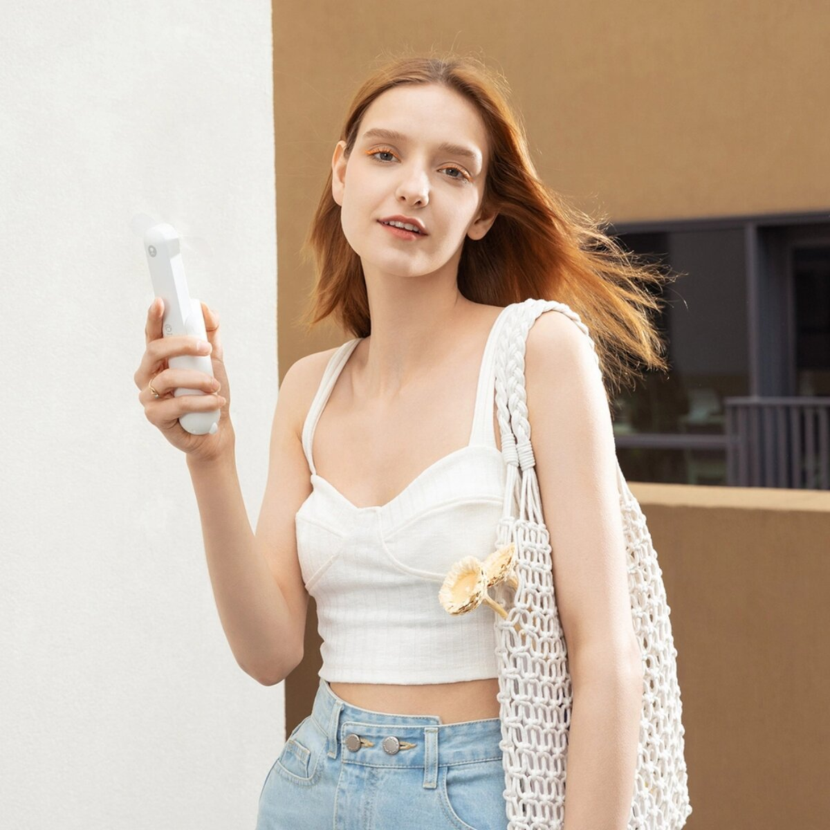 Una giovane donna dai capelli rossi tiene un ventilatore portatile bianco.