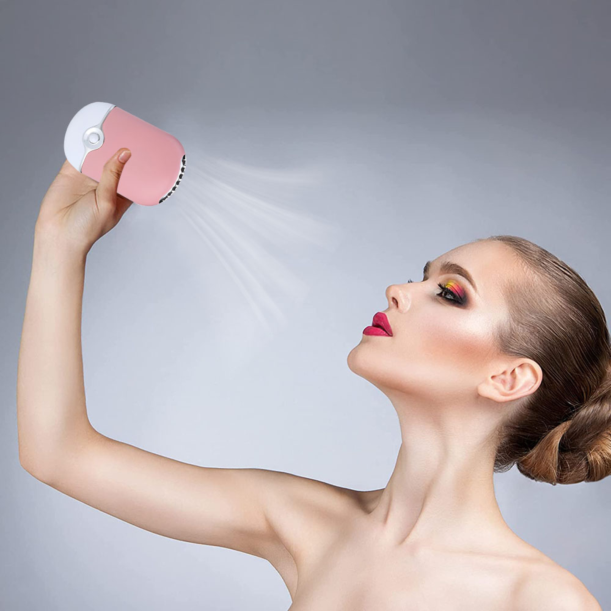 Eine Frau hält einen rosa Mini-Ventilator, der Luft auf ihr Gesicht bläst.