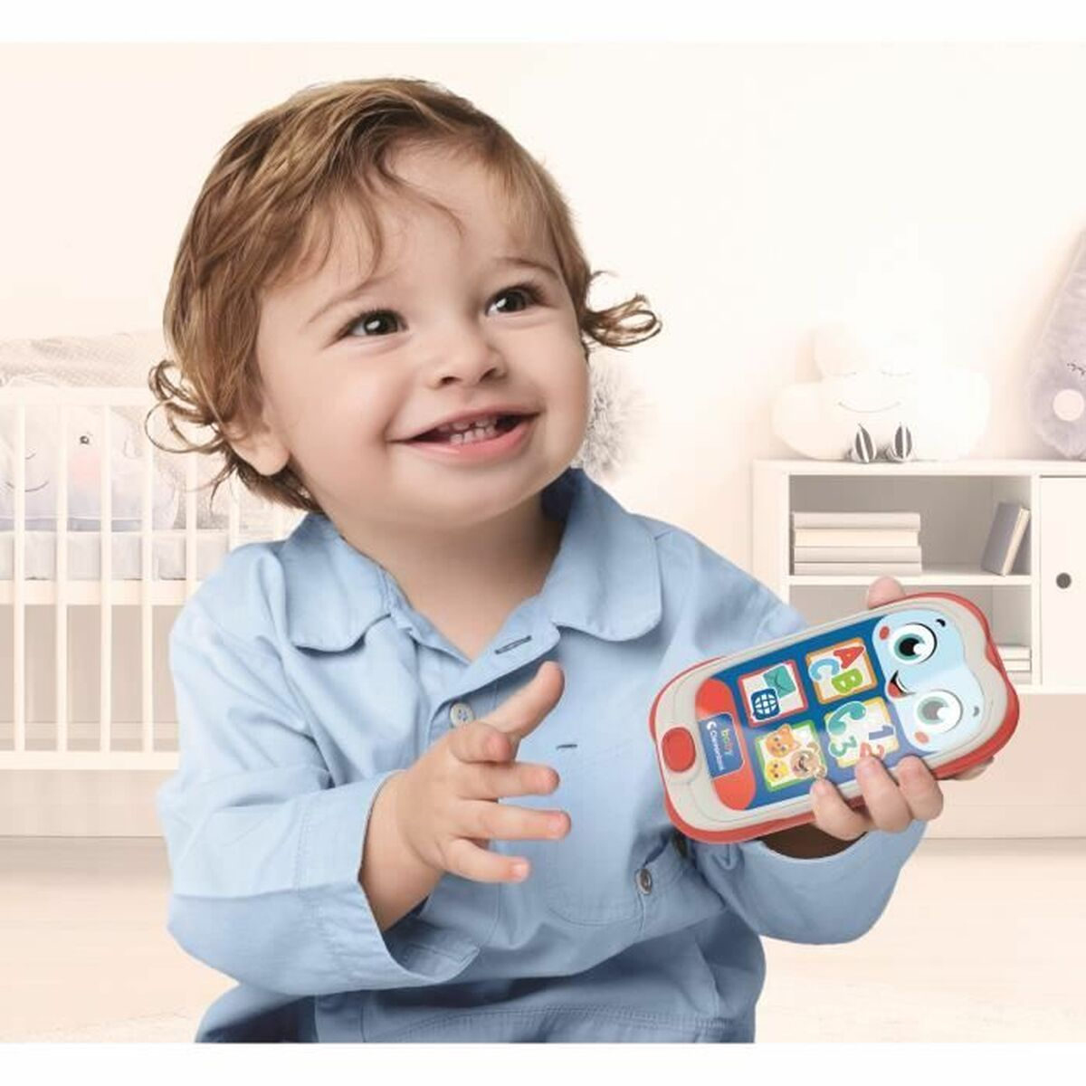 Un bambino sorridente in camicia blu tiene un telefono giocattolo colorato con numeri e lettere.