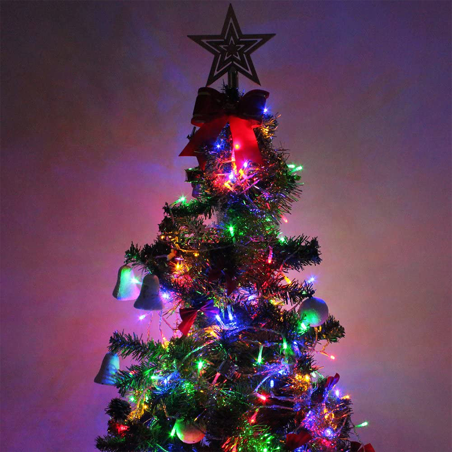 Un albero di Natale decorato con luci, stella, fiocco e campane.