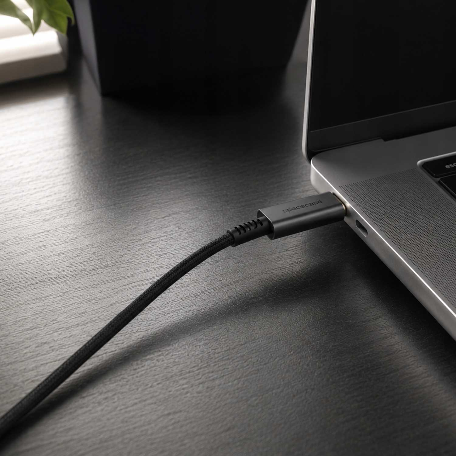 Szary kabel ładujący podłączony do laptopa na ciemnym drewnianym biurku.