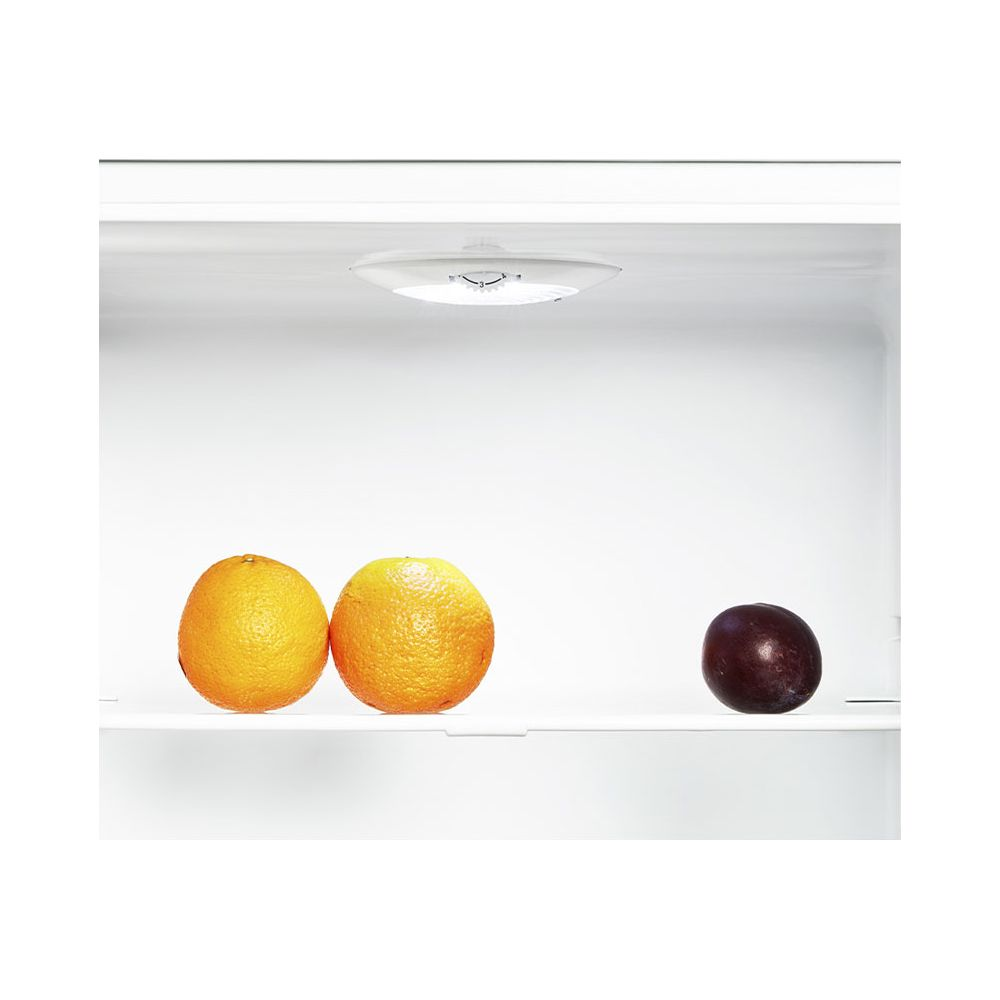 Deux oranges et une prune sur une étagère blanche.