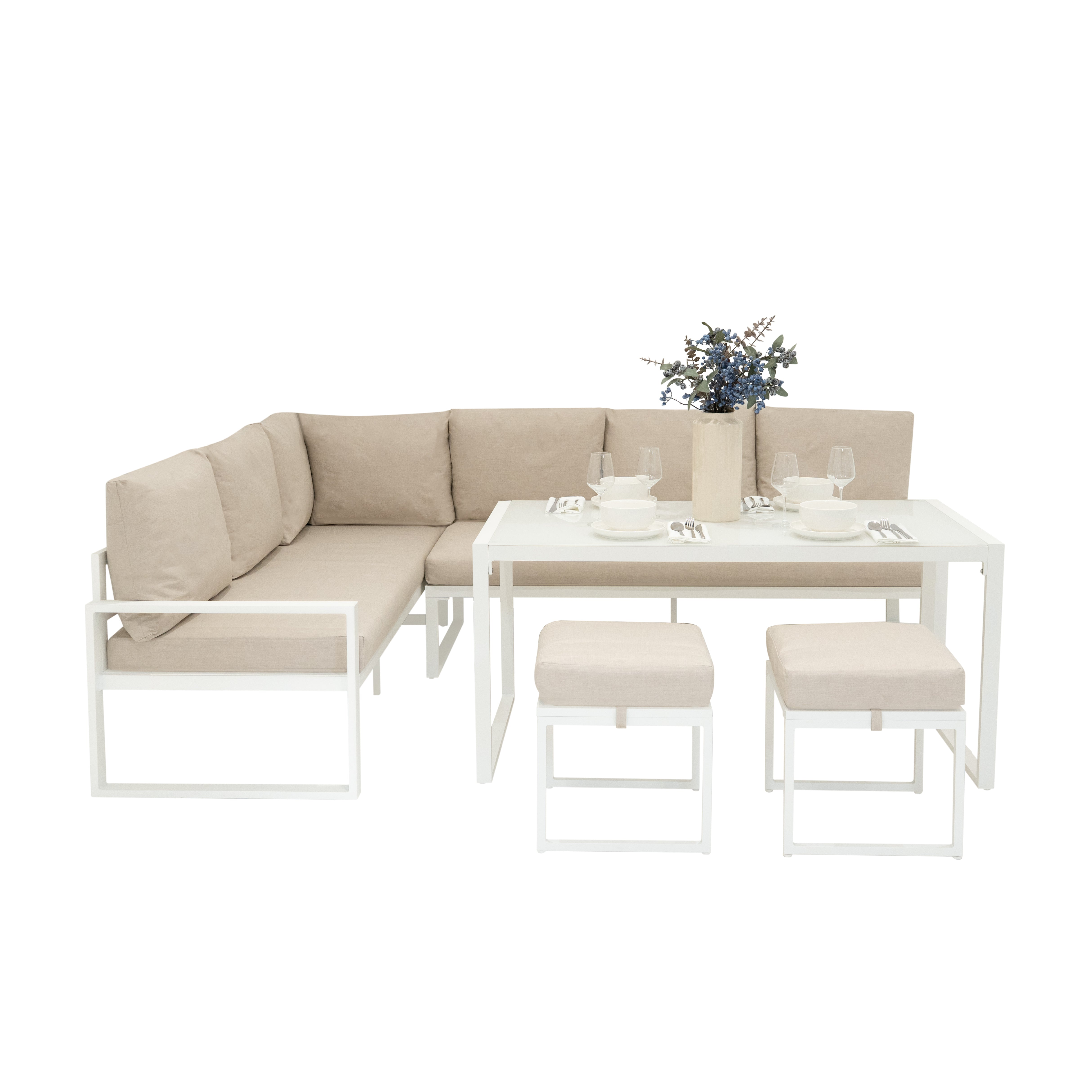 Sofá modular beige con mesa blanca, dos taburetes, vajilla y jarrón con bayas.