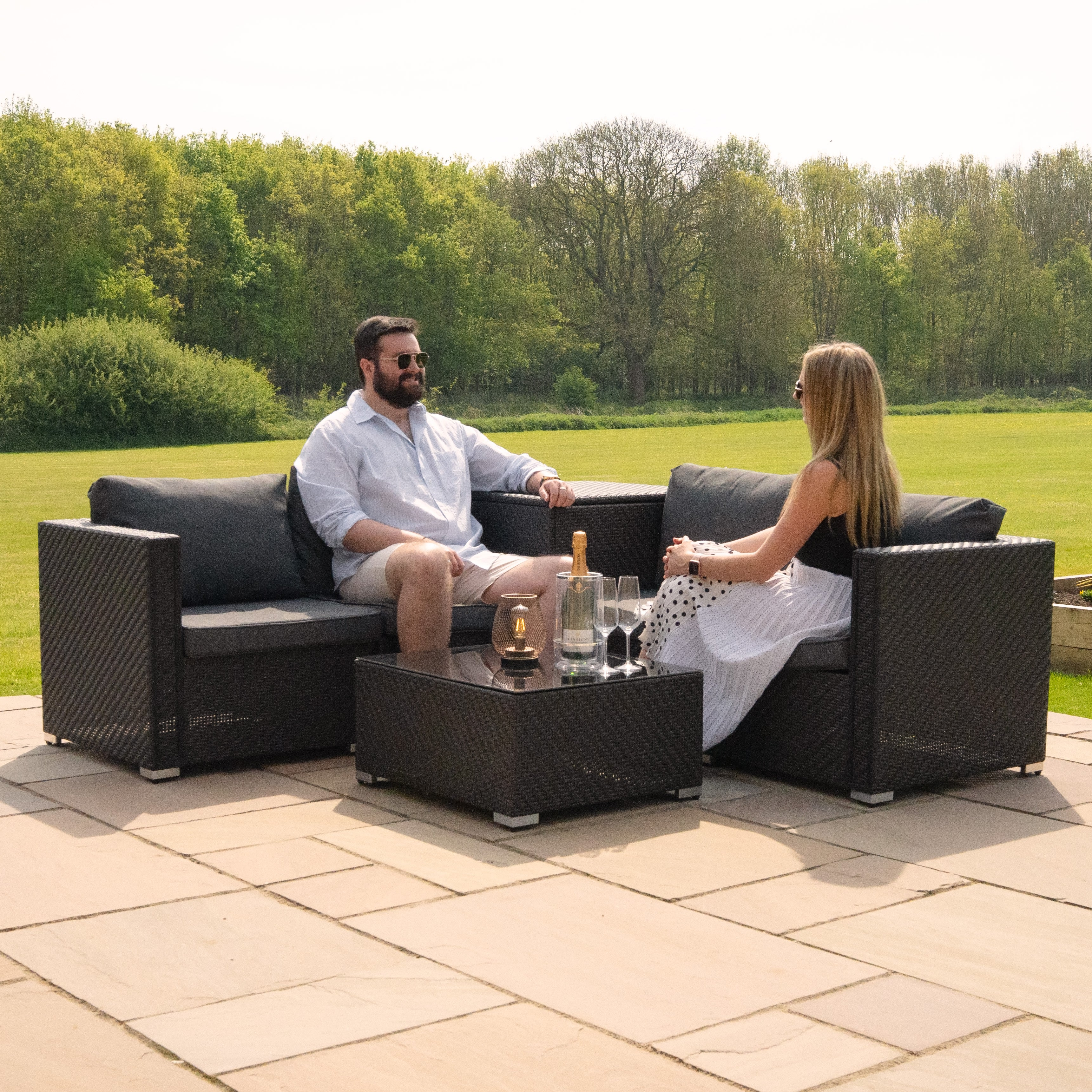 Pareja relajándose en muebles de salón oscuros al aire libre con champán.