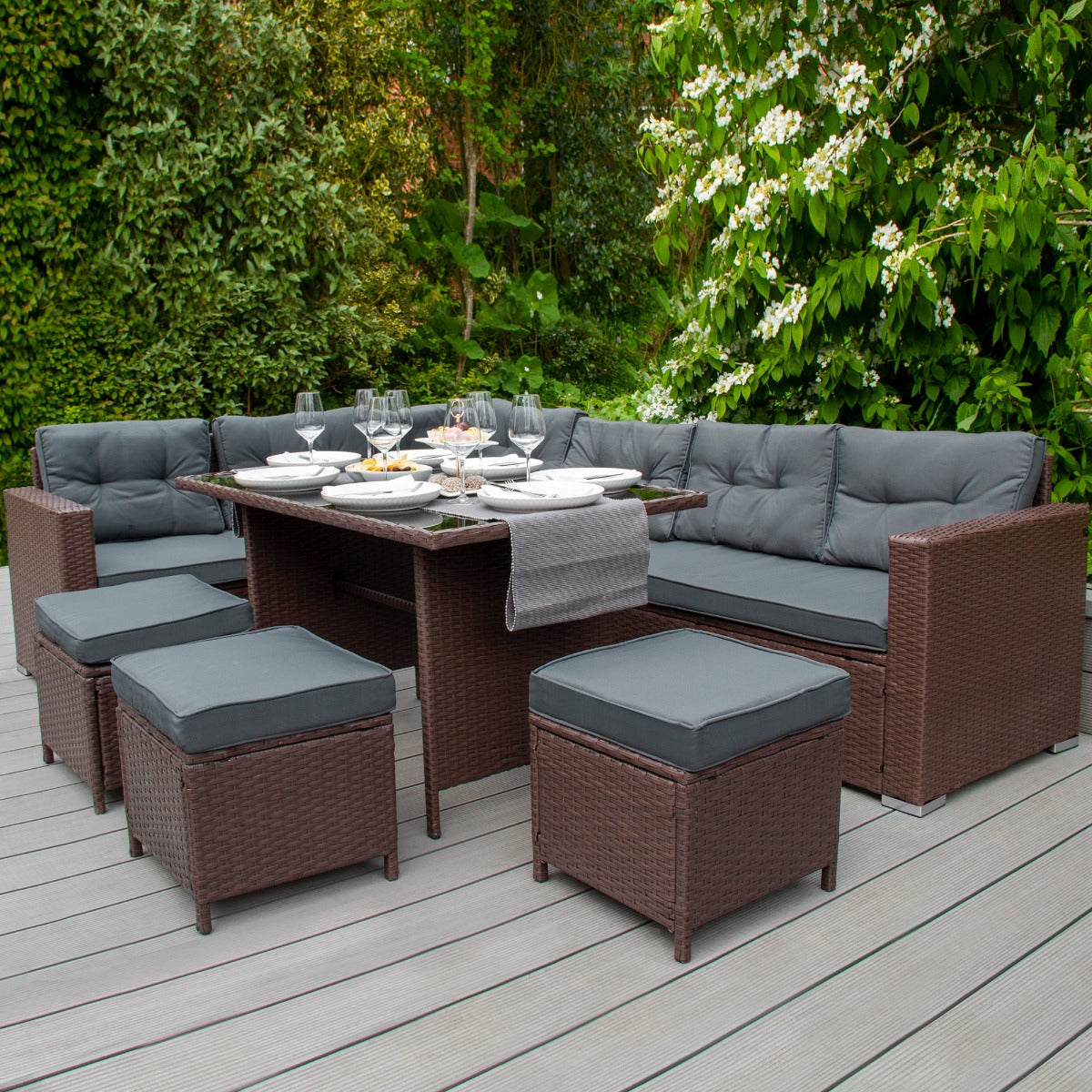 Conjunto de comedor exterior con sofá de ratán y taburetes, rodeado de follaje verde.