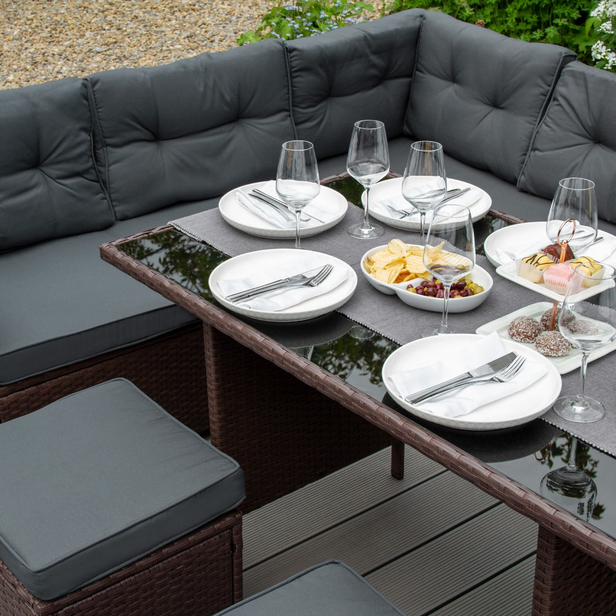 Conjunto de comedor exterior con cojines gris oscuro, mesa puesta para cuatro con aperitivos y bebidas.